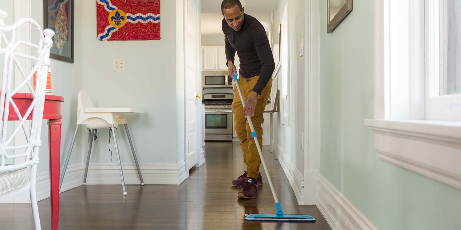 A man cleaning a hardwood floor with a blue sweeper